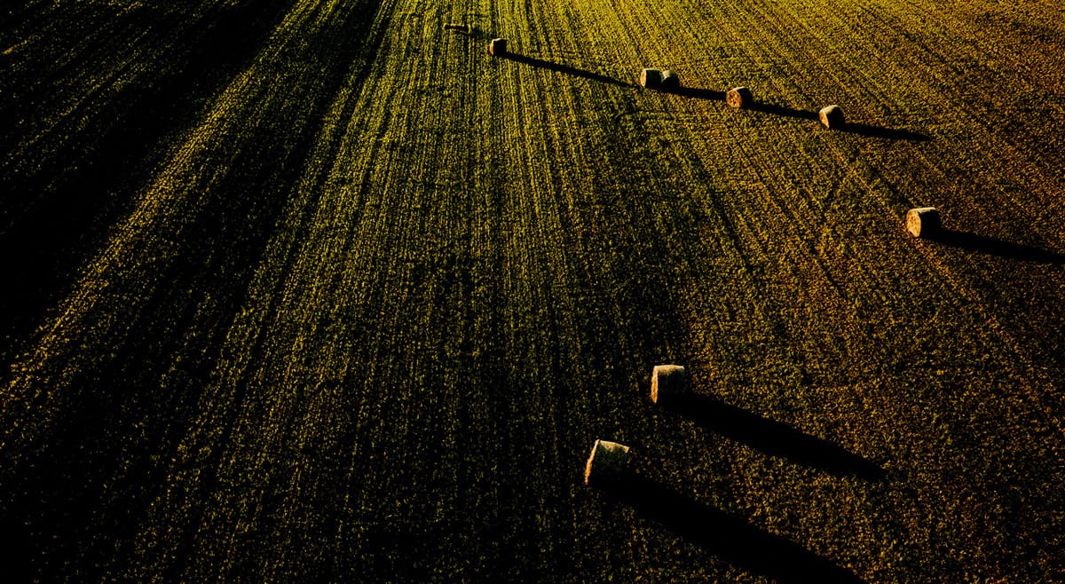Szántóföld szénabálákkal naplementében, precíziós mezőgazdaság támogatásával.