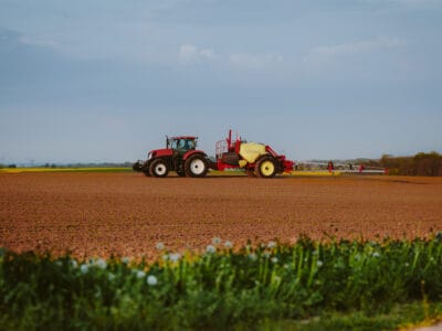 Vörös traktor permetező géppel egy frissen művelt szántóföldön – digitális gazdálkodás az eGN segítségével.